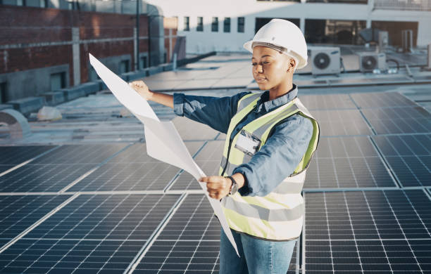 Female engineer, solar panel blueprint or outdoor on roof for power, sustainability plan and energy development. Black woman, photovoltaic tech and reading on rooftop, building or electricity in city
