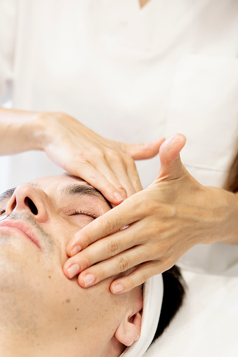 close-up of a beautician's hands performing a facial massage on a middle-aged man, skincare concept