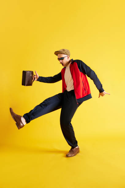 Man in tracksuit holding purse in hands and dancing against yellow background. Man in tracksuit holding purse in hands and dancing against yellow background. Concept of emotions, lifestyle, job and hobbies 21st century style stock pictures, royalty-free photos & images