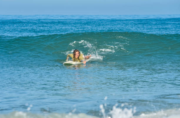 istock Young woman paddling to catch a wave while surfing 1613828405