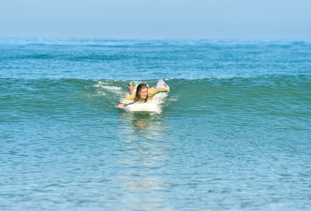 istock Young woman paddling to catch a wave while surfing 1613830070