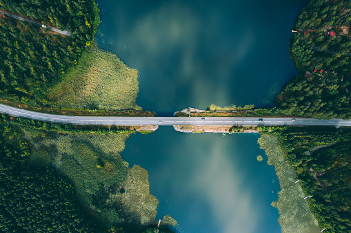 Aerial view of bridge asphalt road with cars and blue water lake and green woods. Beautiful summer landscape in Finland.