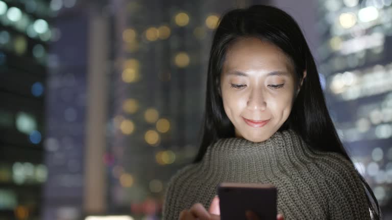 Woman using smart phone over office building at night