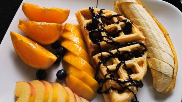 Delectable Breakfast: Drizzling Vienna Waffles and Fresh Fruits with Chocolate Syrup. Enjoy delightful morning feast as rich chocolate syrup is poured generously over Vienna waffles and fresh fruits