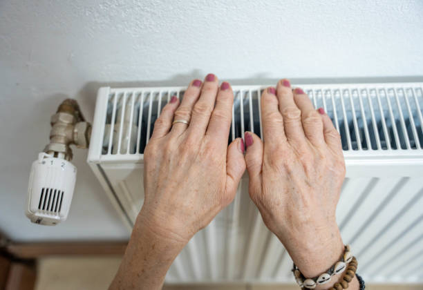 istock Women warming hands on heating radiator near white wall 1613871862