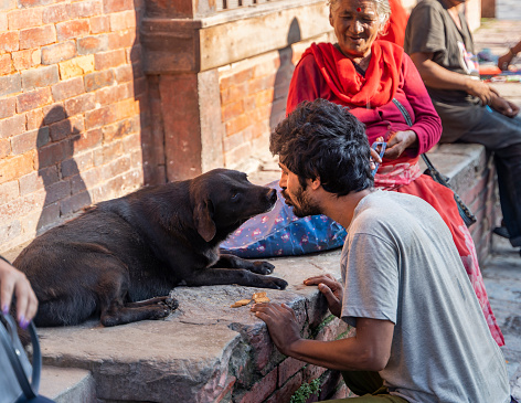 Kathmandu, Nepal - August 04, 2022: People of Nepal. Man feeding stray dog and old woman smiling in the background.