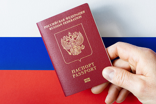 A man's hand holds a International passport of the Russian Federation on a background of national flag