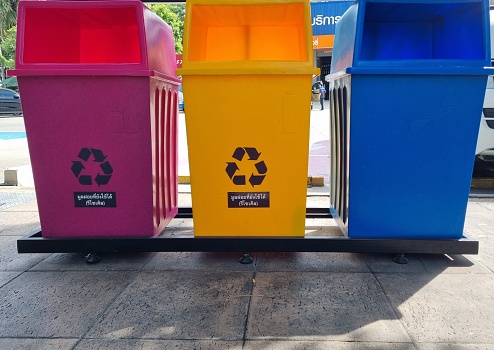 Three recycling bins, red, yellow and blue, are located along a street in the city.