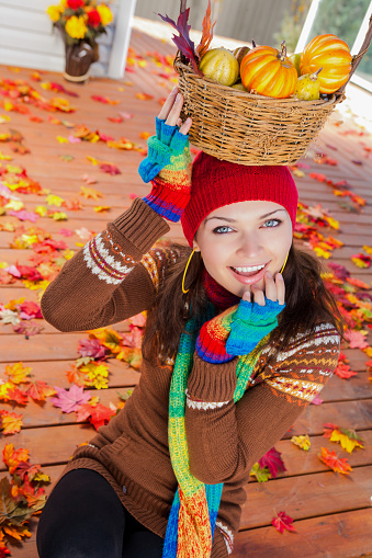 Smiling beautiful Ukrainian woman playful holding basket of pumpkins on her head