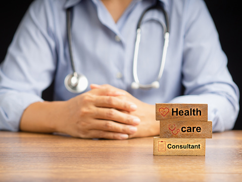 Wooden blocks with the letters Health, Care, and Consultant over a wooden desk with a doctor sitting blurred background. Medical and healthcare concept