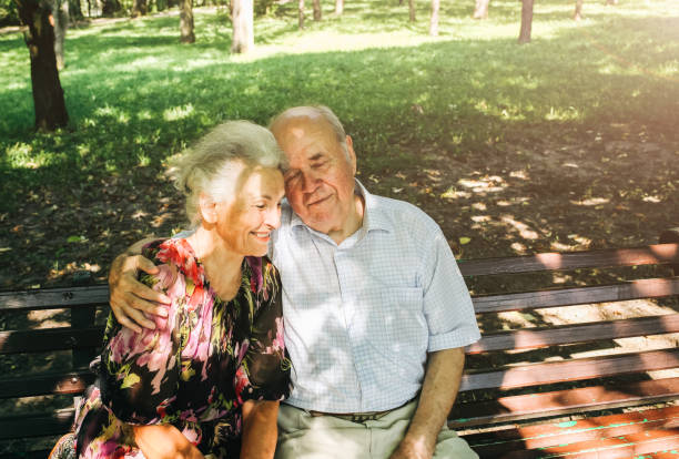 schönes altes paar sitzt auf der bank im park. oma und opa umarmen sich im freien. herzlichen glückwunsch zur goldenen hochzeit. romantisches foto von großmutter und großvater. echte liebe. - senior adult women park bench 70s stock-fotos und bilder