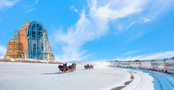 Red diesel train (East express) in motion at the snow covered railway - Horses pulling sleigh in winter - Ani Ruins, Ani is a ruined and  medieval Armenian city - Kars, Turkey