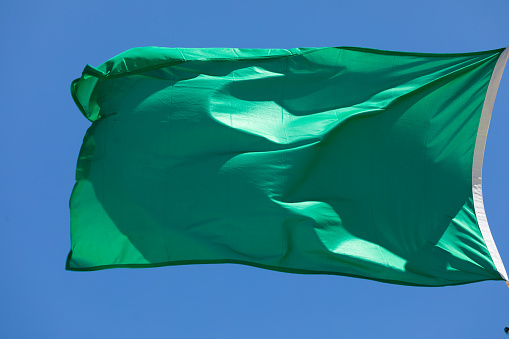 Green flag of the lifeguard service, waving in the wind on a beach in Spain in summer, indicates that it is safe to swim