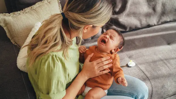 Photo of Young mother tries to calm her screaming newborn baby