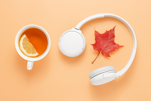 Wireless headphones with autumn leaf and cup of tea with lemon. Learning and education concept, listening audio books, music or online courses, studying or home office work, cozy fall concept