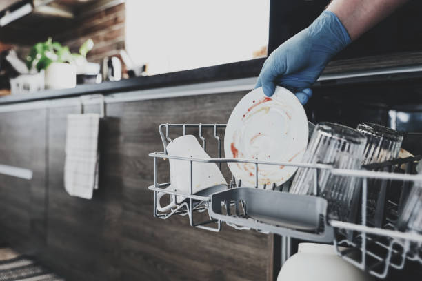 woman hand is loading dirty utensil to opened dishwasher machine at kitchen - water human hand stream clean imagens e fotografias de stock