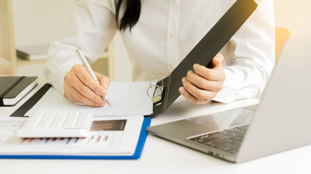 istock Female accountant analyzing charts, graphs, computer, investment tablet and pressing calculator button above document. Accountants, accountants, clerks, bank consultants and auditors. close-up photo 1614080890