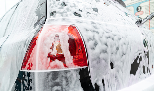 The taillight and trunk of the car are coated with white detergent. Close-up. The car covered in white foam at a self-service car wash.