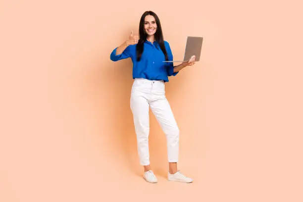 Photo of attractive satisfied lady it specialist wear stylish outfit hold macbook thumb up good feedback isolated beige color background.