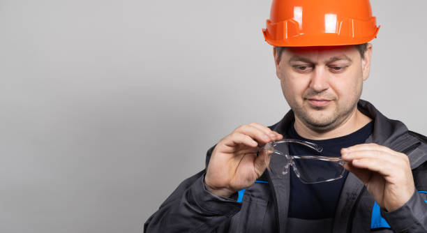 istock A construction worker in a helmet and overalls put on goggles protective glasses on a white background. 1614128070