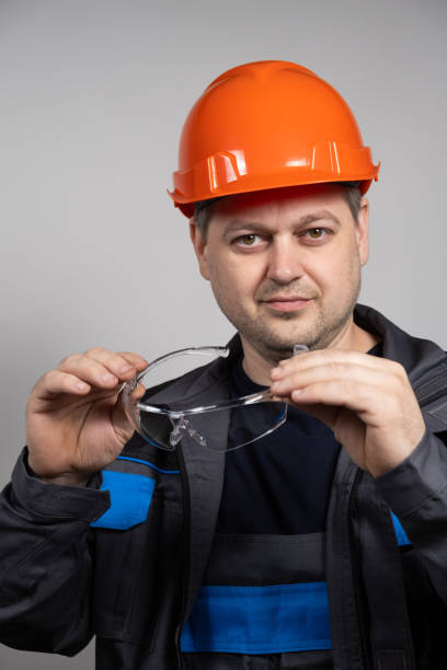 istock A construction worker in a helmet and overalls put on goggles protective glasses on a white background. 1614128071