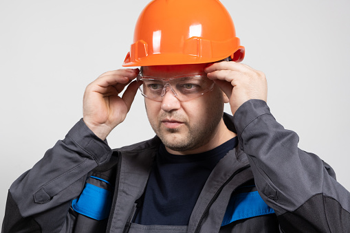 Portrait of a handsome worker builder in overalls, helmet and glasses on a white background