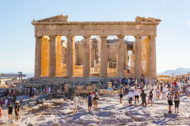 Crowds of tourists visit everyday the Parthenon in the Acropolis in Athens, Greece. At sunset heat decreases and shadows are long.