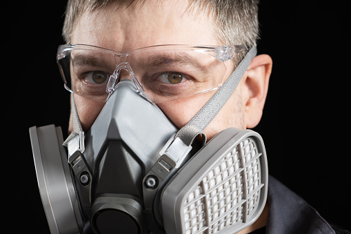 Portrait of a man in a protective respirator, a mask with dust and gas filters, on a black background