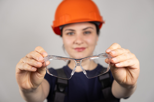 A woman, a builder or engineer, holds goggles on a white background.