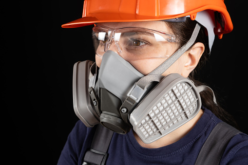 A woman wearing a helmet, respirator and goggles on a black background.