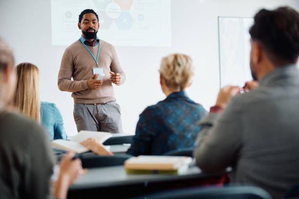 Black teacher talking during presentation on adult education training class. African American adult education teacher giving a lecture to group of students in the classroom. teacher projector stock pictures, royalty-free photos & images