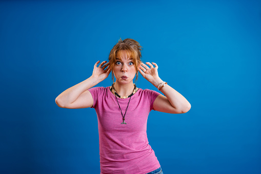 Portrait of a beautiful young woman making a funny face while standing in front of a bright blue background.
