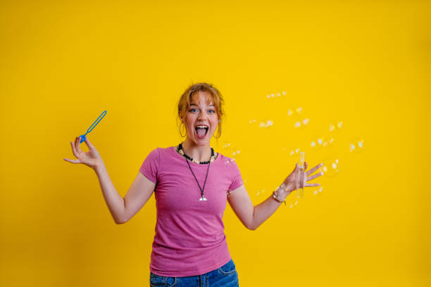 istock Happy Young Woman Blowing Bubbles Against A Yellow Background 1614167551