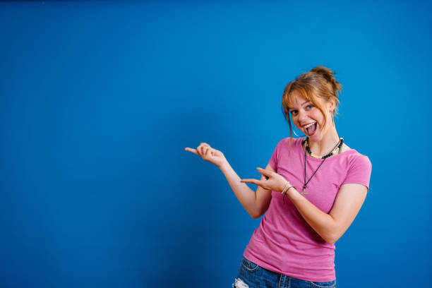 Portrait of a beautiful young woman pointing with her finger while standing in front of a bright blue background.
