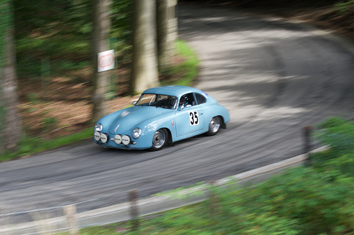 08 13 2023
Theux Belgium.
Old mythical Porsche of 1956 driving at full speed on a country road in a Belgian race called (the climb of the maquisard) with a motion blur.