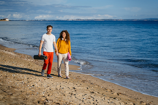 Beautiful young couple with exercise mats walking on the beach in Nea Flogita, Greece.