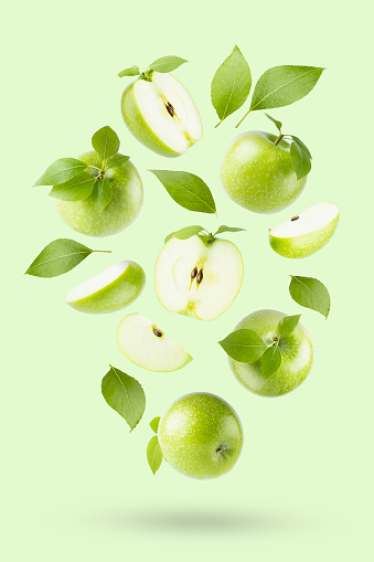 Juicy green apples with green leaves fly or fall on light green background as art composition, with whole, half, quarter fruit, isolated, shadow. Summer fruits for advertising, design, label product.