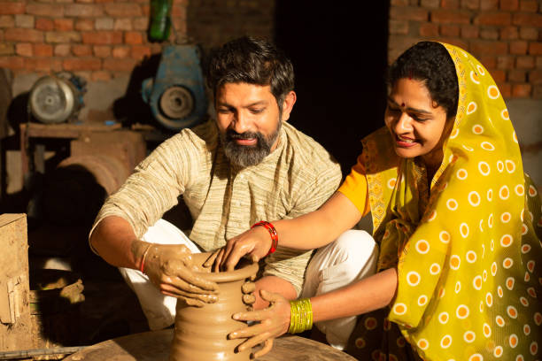istock Traditional indian woman pottery maker helping and supporting her husband working with clay pot, skill india concept. 1614208691