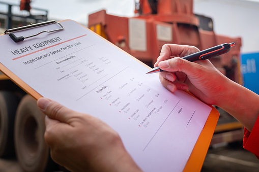 A mechanical engineer is inspecting the condition of truck crane vehicle (as blurred background) before start the operation on the inspection checklist form. Industrial working with safety practive.