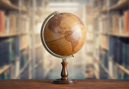 Old geographical globe and old book in cabinet with bookselfs. Science, education, travel background. History and geography team. Ancience, antique globe on the background of books.