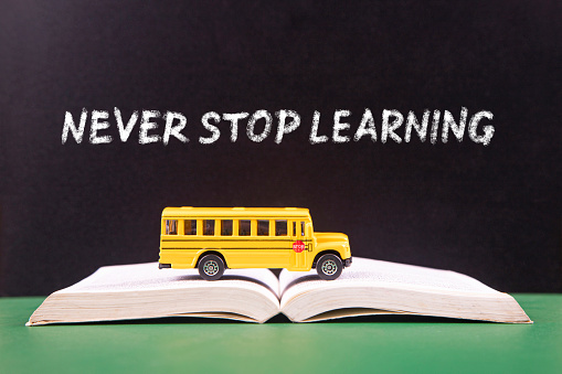 Yellow retro school bus on book and text Never stop learning