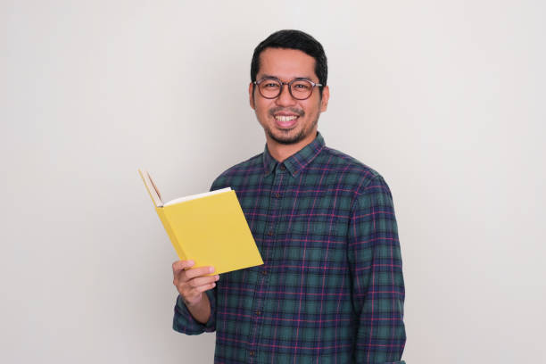 istock Adult Asian man smiling confident while holding a book 1614298531