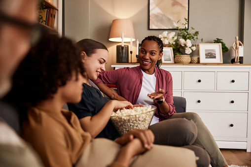 A smiling African woman talking with friends while eating popcorn and watching a movie in the living room.
