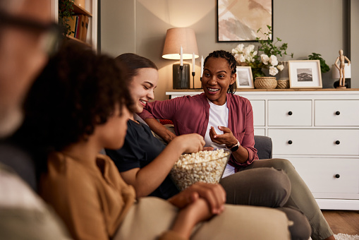 A pretty African-American female sitting with friends on a couch, having fun eating popcorn.