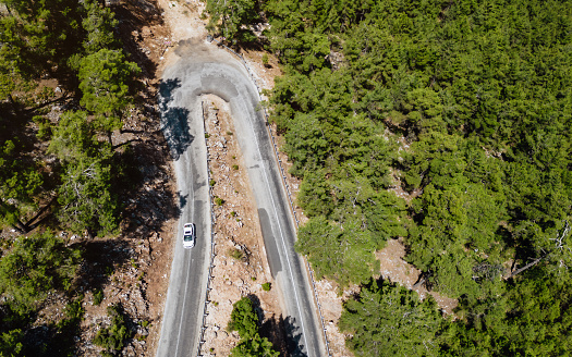 Mountainous region covered with pine forest.A bird's-eye view shot with drone.Vehicle driving on asphalt road.Nature road landscape