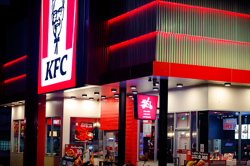 Corner and windows of KFC restaurant in Bangkok at night. Scene is at KFC at Wanghin Road in Bangkok Ladprao. Inside are customers and people