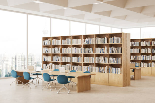 istock Cozy library interior with bookshelves and desk with laptop, window 1614334896