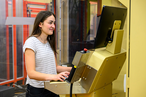 Smiling young woman working at a big CNC machine in a workshop