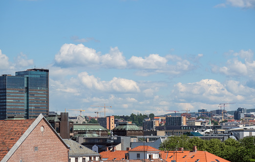 View over a part of the skyline of the Norwegian capital Oslo, featuring numerous buildings and cranes, a vast expanse of blue sky, and much copy space