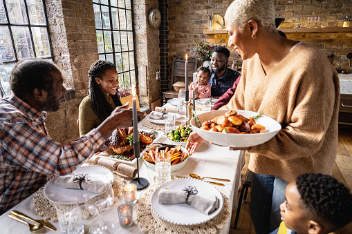 Elegant dining table with lit candles, Christmas cracker by each place setting, roast turkey, potatoes, root vegetables, and smiling family members.